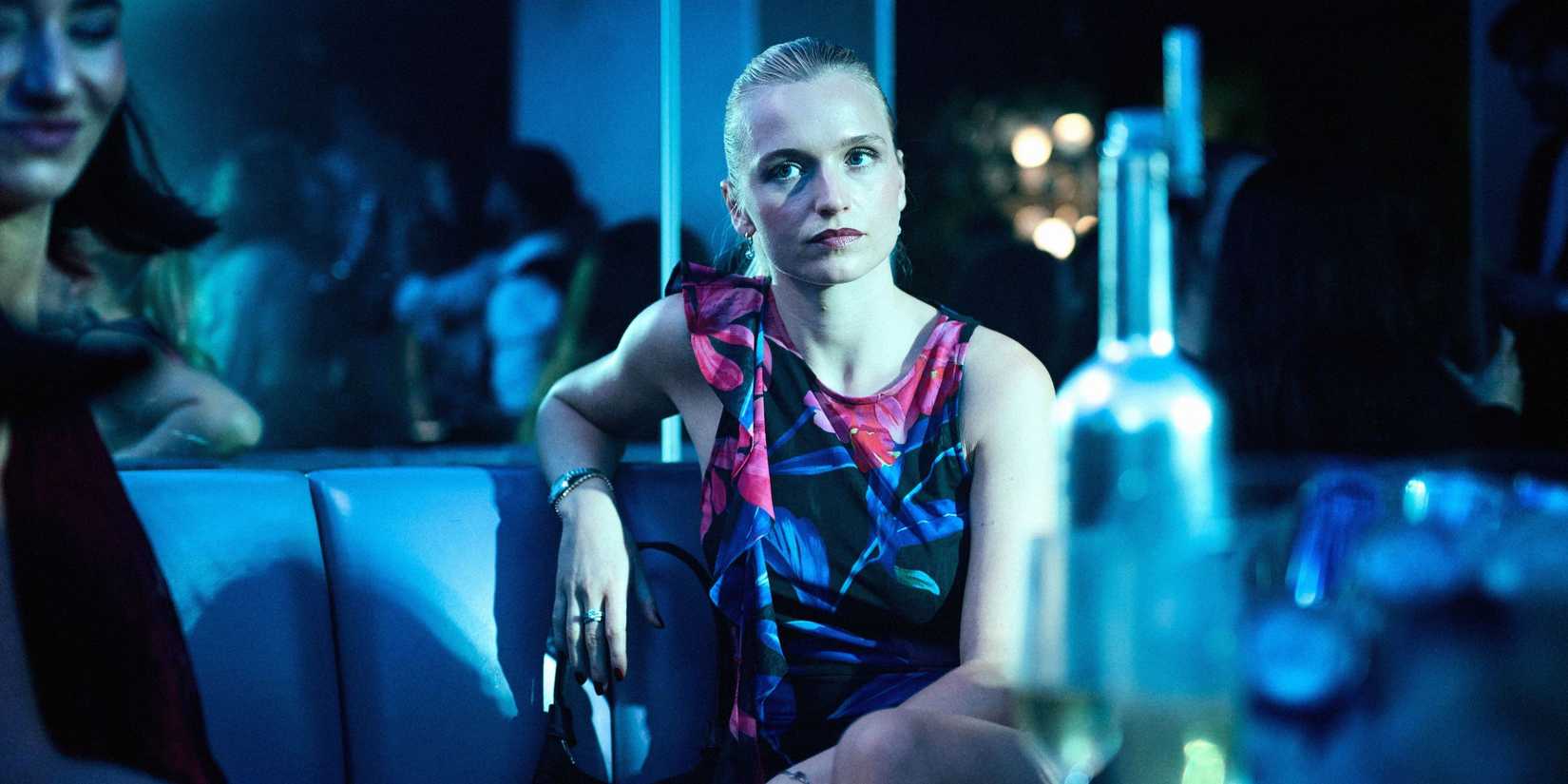 Tea (Clara Dessau) olhando com irritação para alguém em um clube na série The Asset.