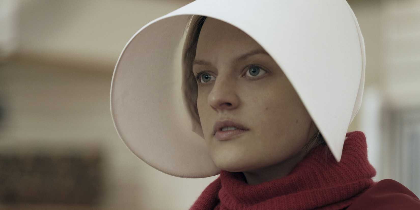 Offred looks concerned while wearing a white hat and red scarf in The Handmaid's Tale