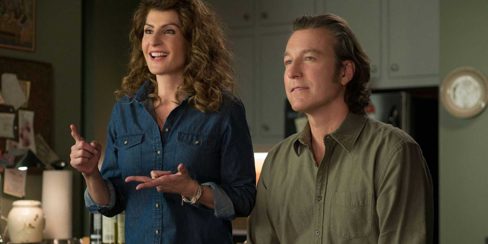 Toula and Ian sitting in a kitchen, having an enthusiastic conversation with someone off-screen, in My Big Fat Greek Wedding 2.