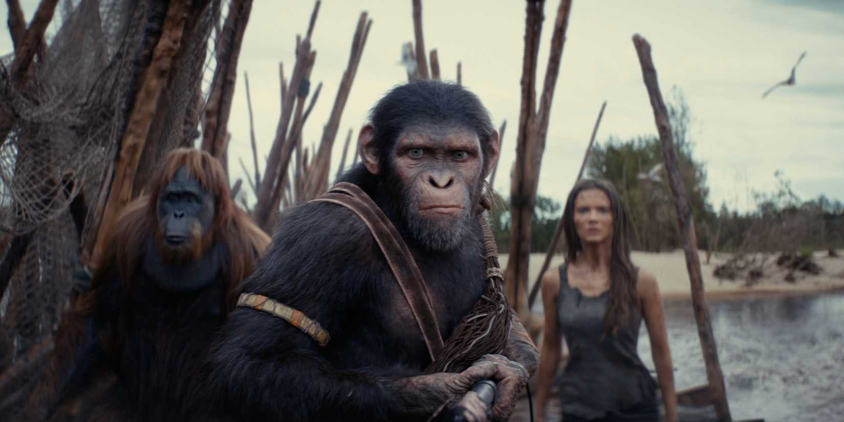 Noa and Raka holding spears and protecting Mae as they pass a body of water in Kingdom of the Planet of the Apes.