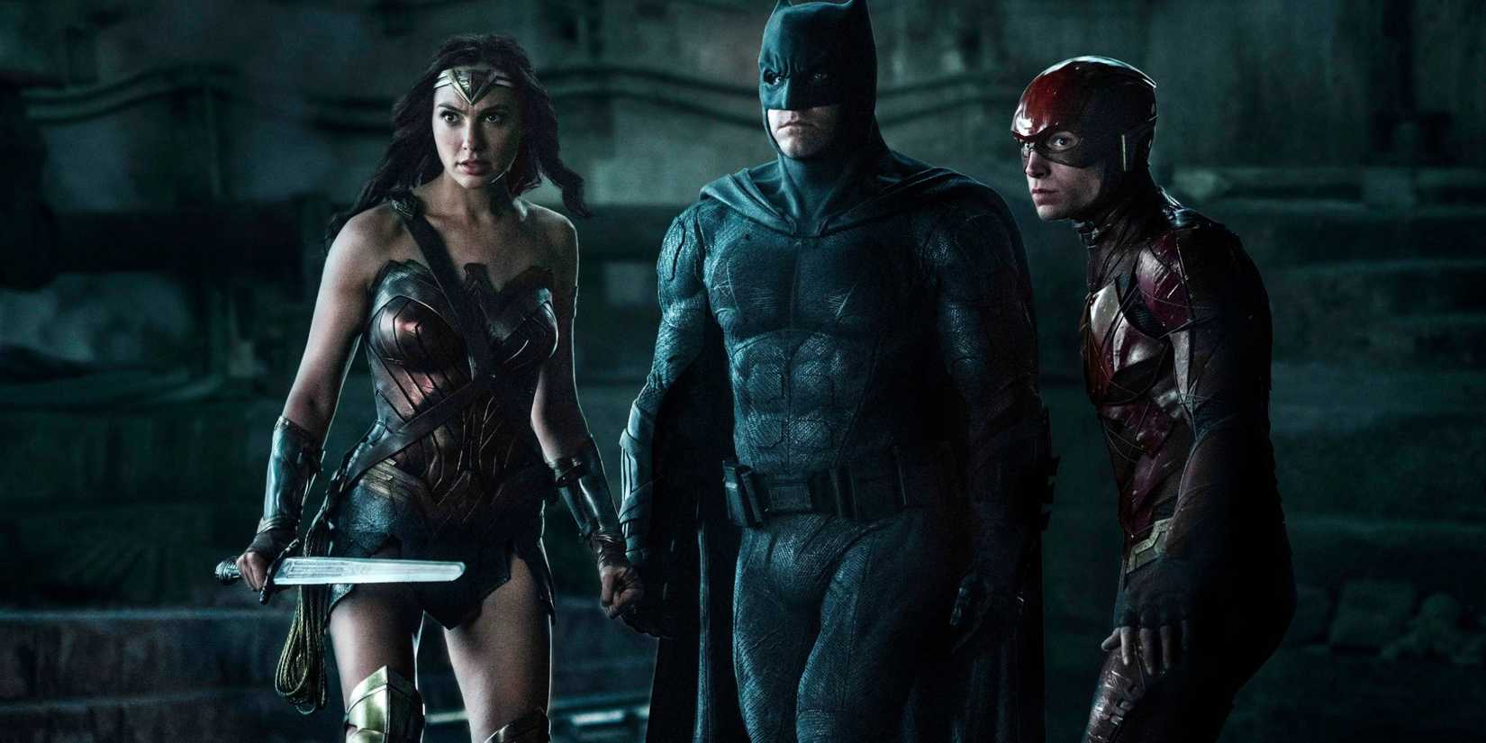 Batman, Wonder Woman, and the Flash looking tense while staring off at something in the darkness in Justice League.