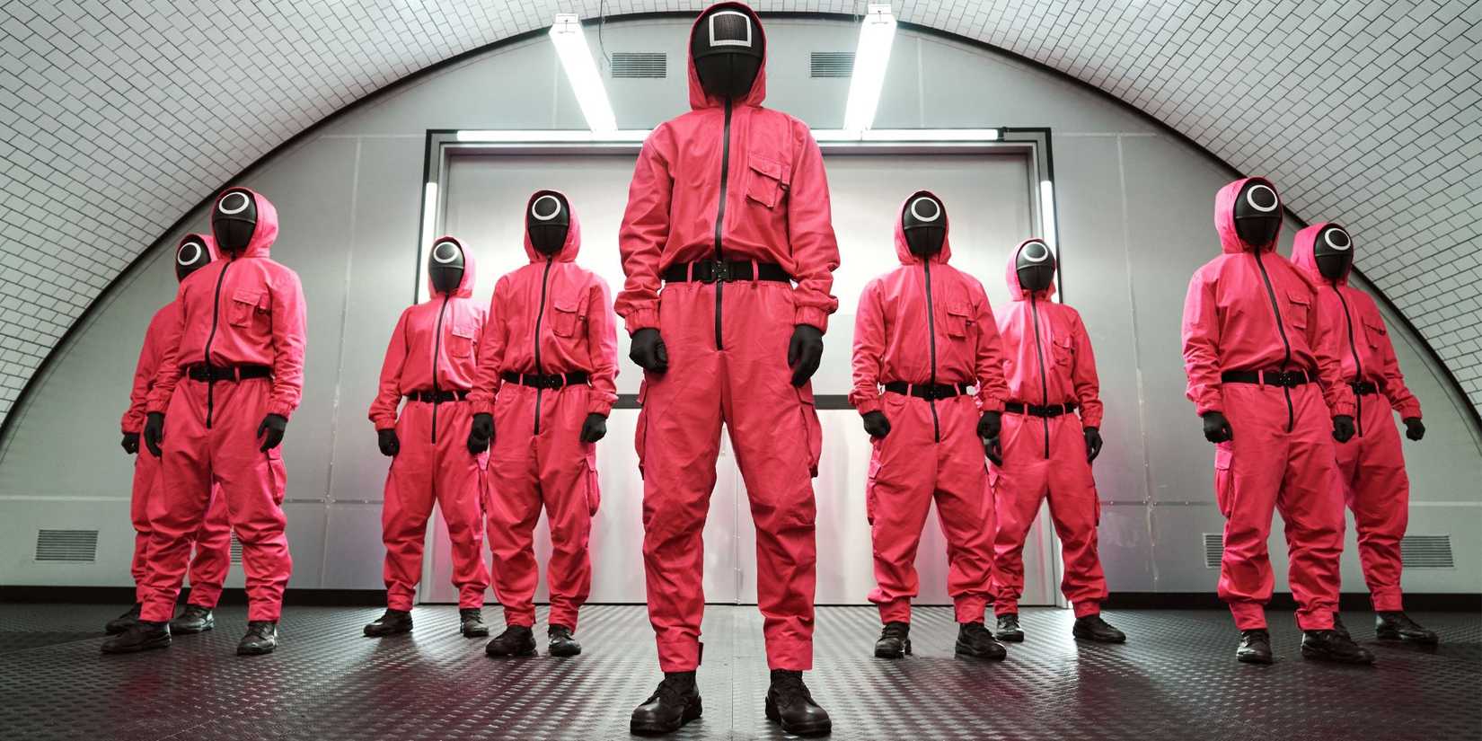 Personagens de Squid Game vestindo macacões vermelhos em cena da série.