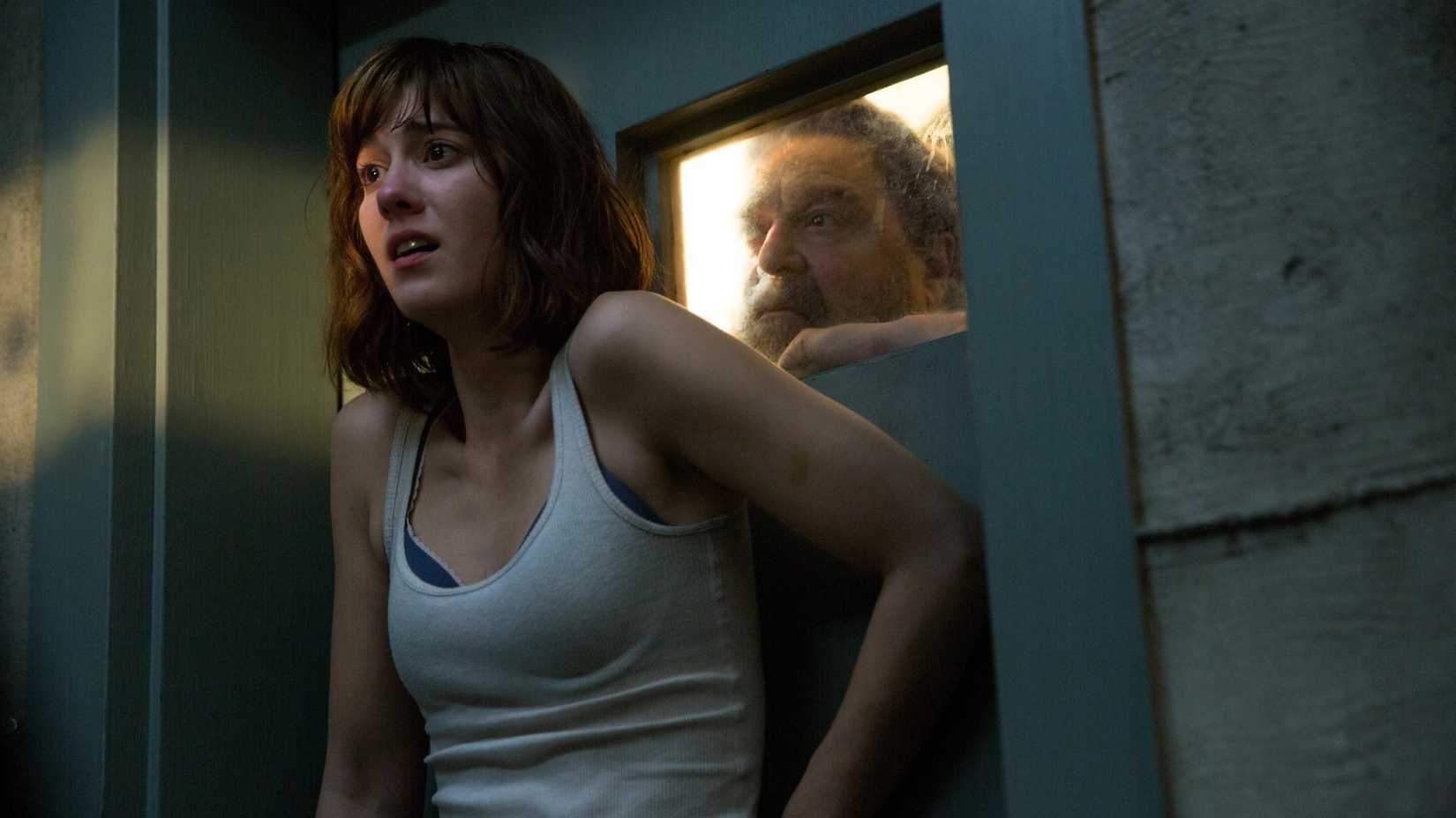 Mary Elizabeth Winstead se encolhe contra uma porta enquanto John Goodman olha pela janela em 10 Cloverfield Lane