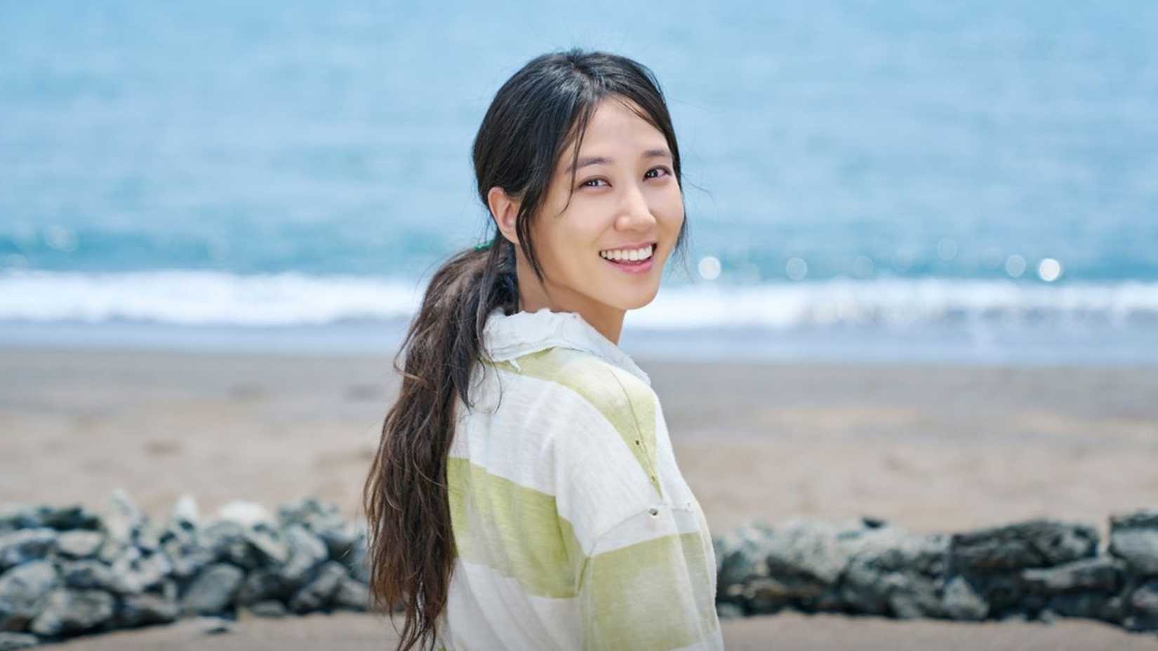 Uma jovem na praia, sorrindo por cima do ombro no K-drama Castaway Diva.