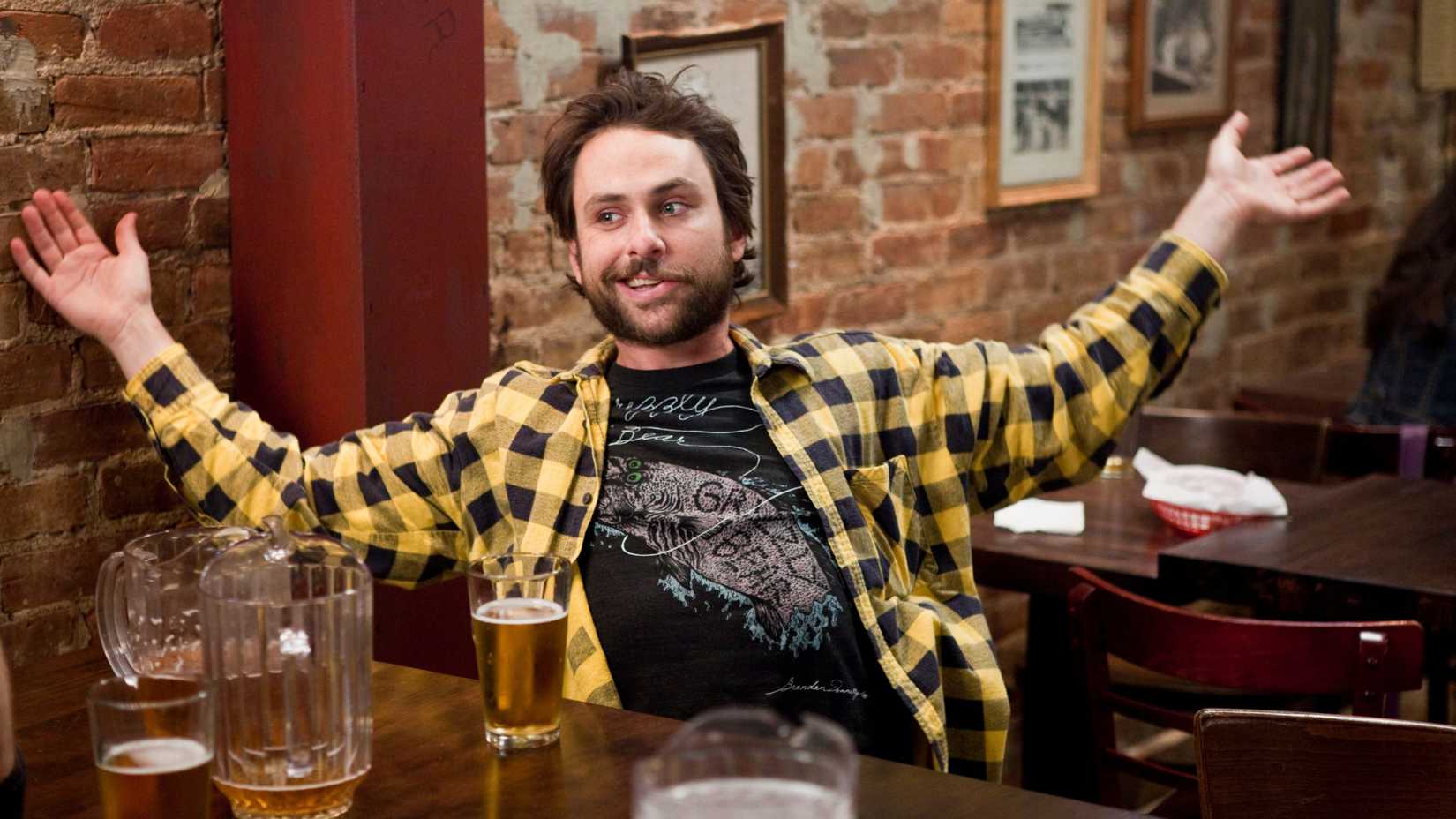 charlie day sitting in paddy s pub with his hands outstretched and a beer on the table in it s always sunny in philadelphia