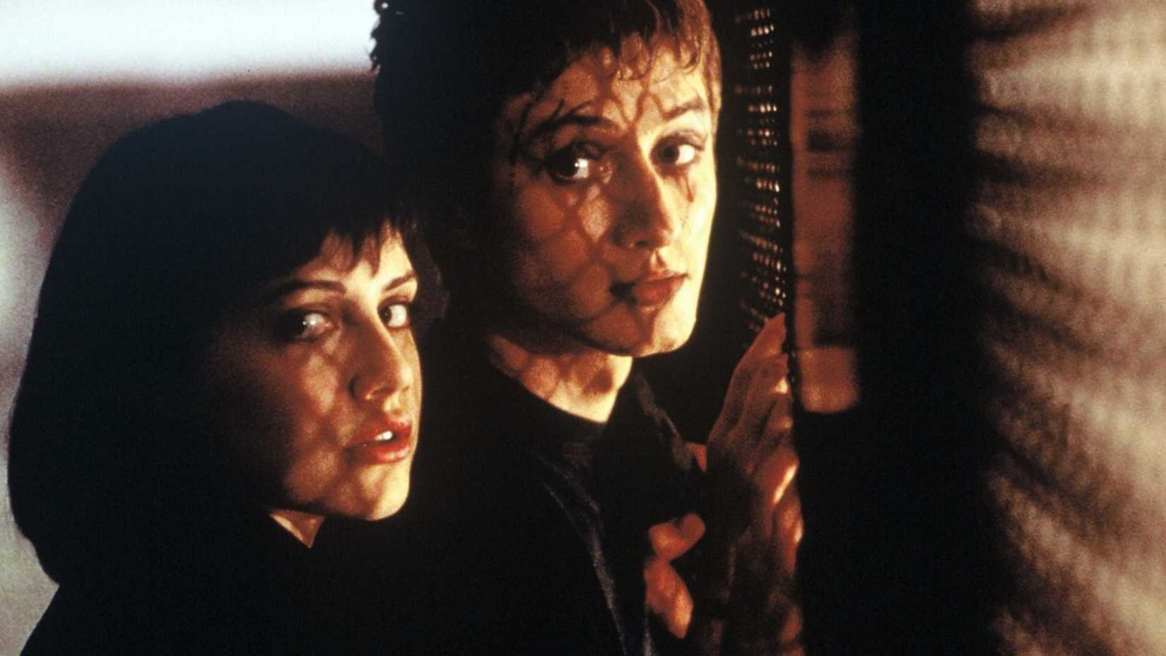 Dois adolescentes olham por cima do ombro enquanto estão perto de uma cerca em Cherry Falls.