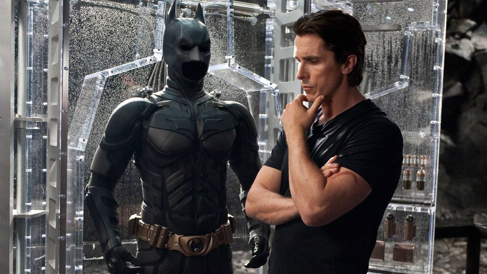 Christian Bale as Bruce Wayne in front of Batman's suit in The Dark Knight Rises