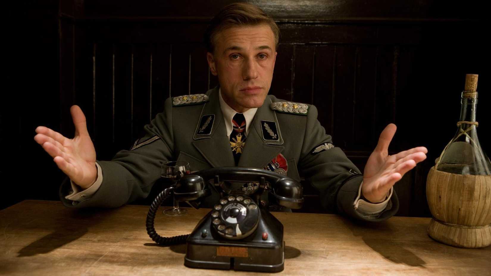 Landa hält seine Hände hoch, während er an einem Tisch in Inglourious Basterds sitzt