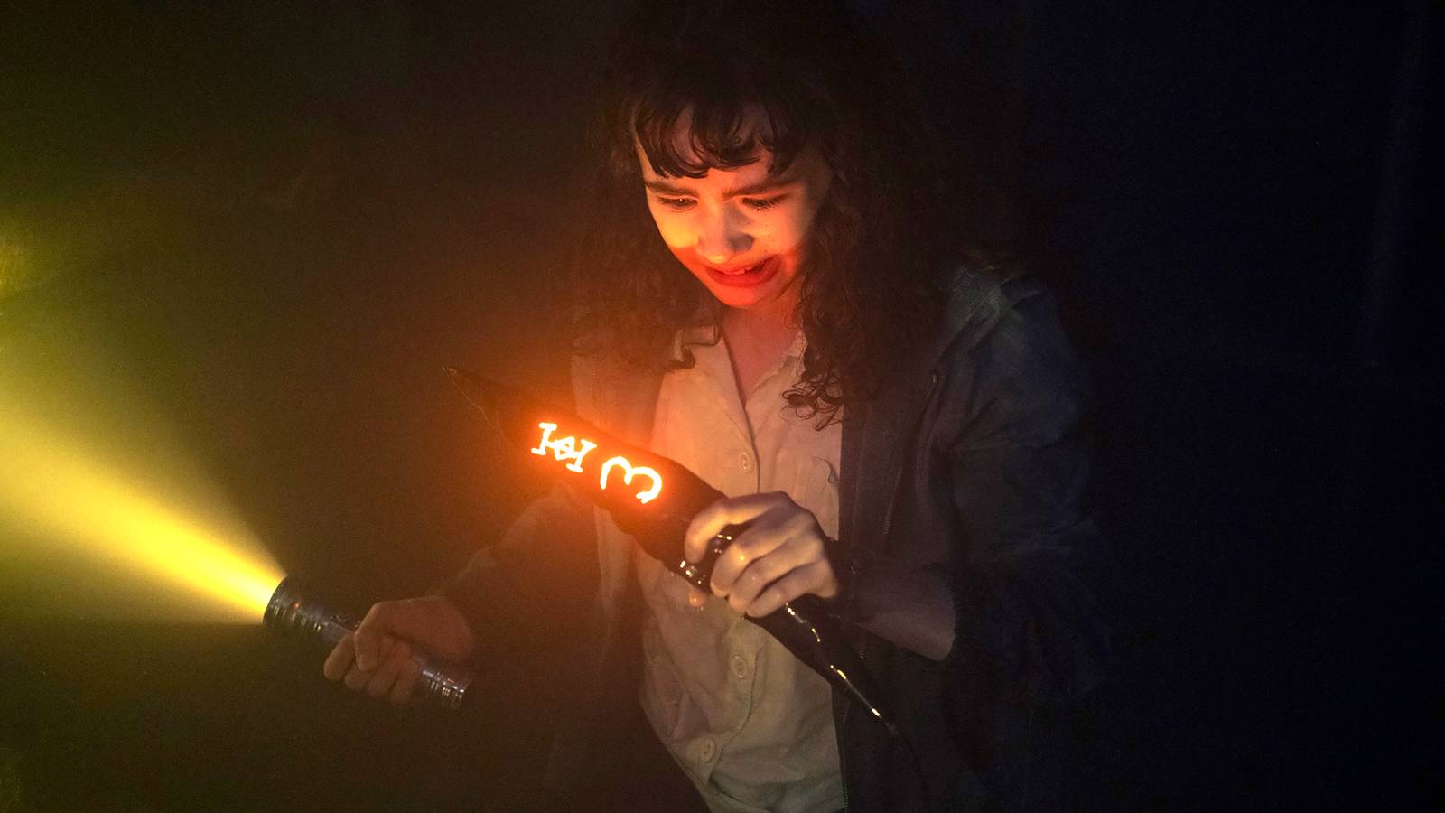 Clara Stack as Lilly looking scared while holding onto glowing shard and a flashlight in IT: Welcome to Derry episode 5