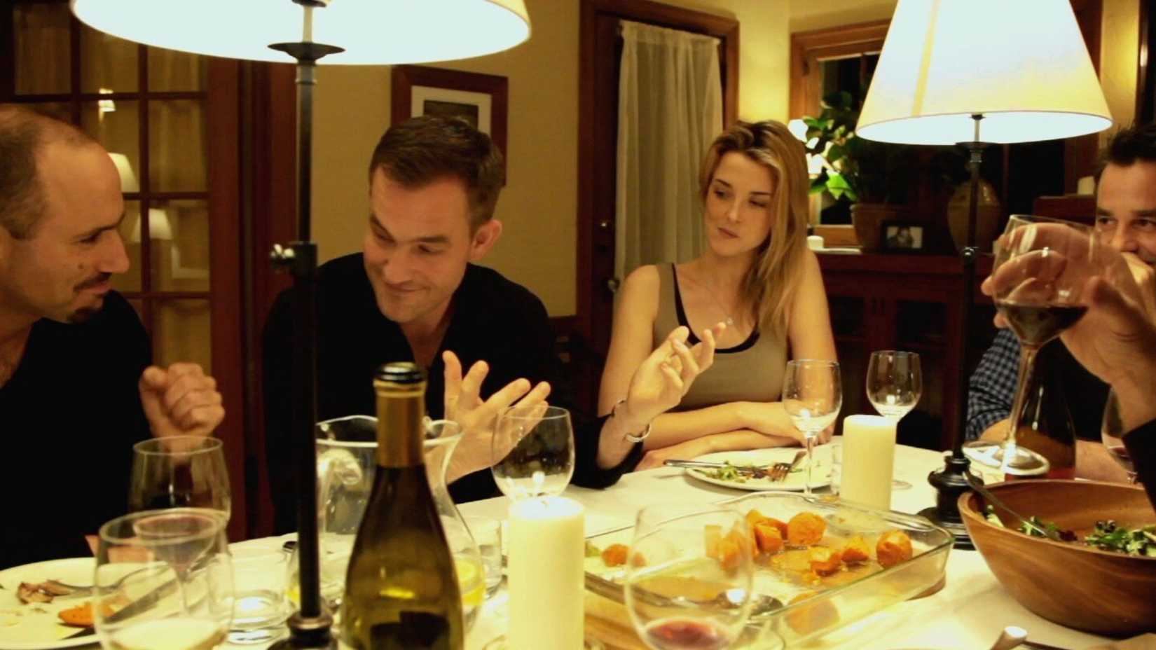 Amigos riem e conversam sentados à mesa de jantar em Coherence