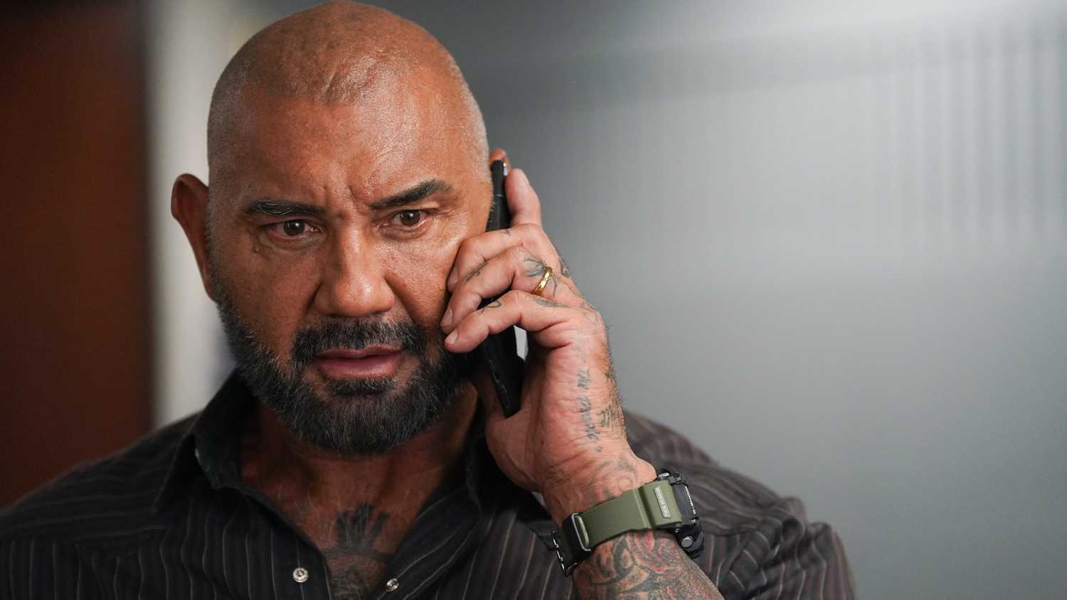 Dave Bautista com olhar intenso enquanto utiliza o telefone em Trap House