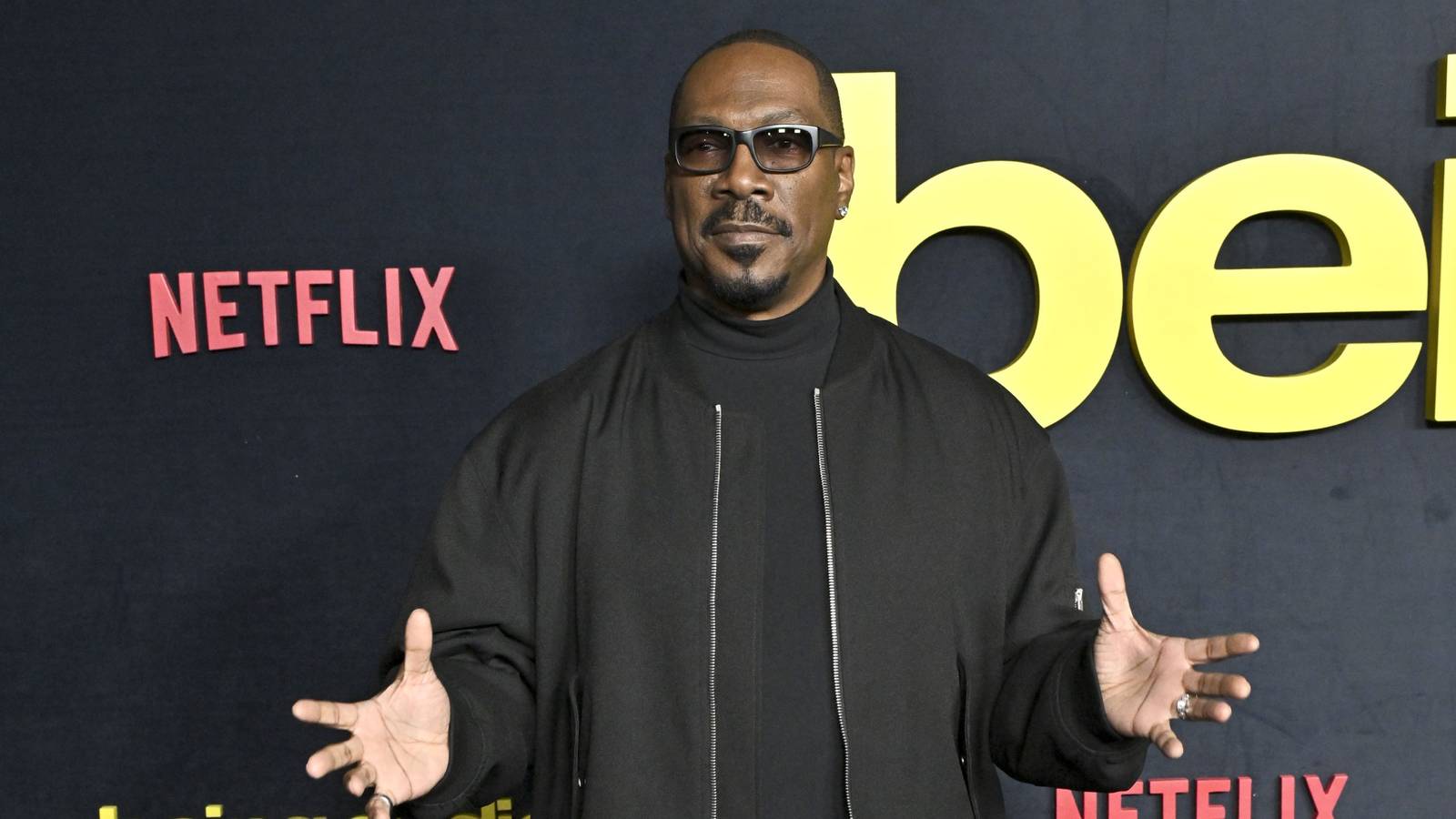 Eddie Murphy stands with his arms out on the red carpet for Being Eddie