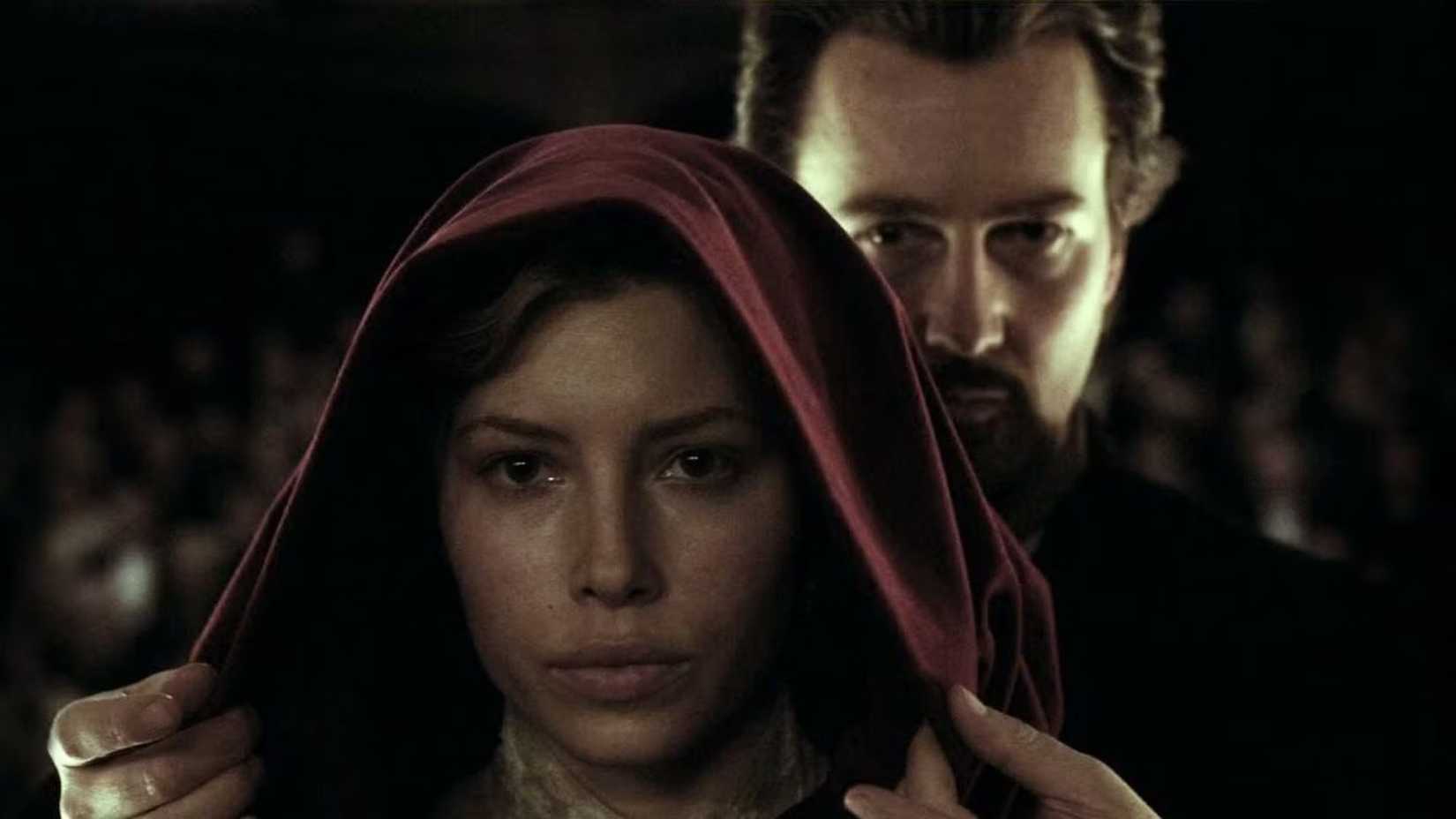 edward norton standing behind jessica biel about to peel back her hood in the illusionist