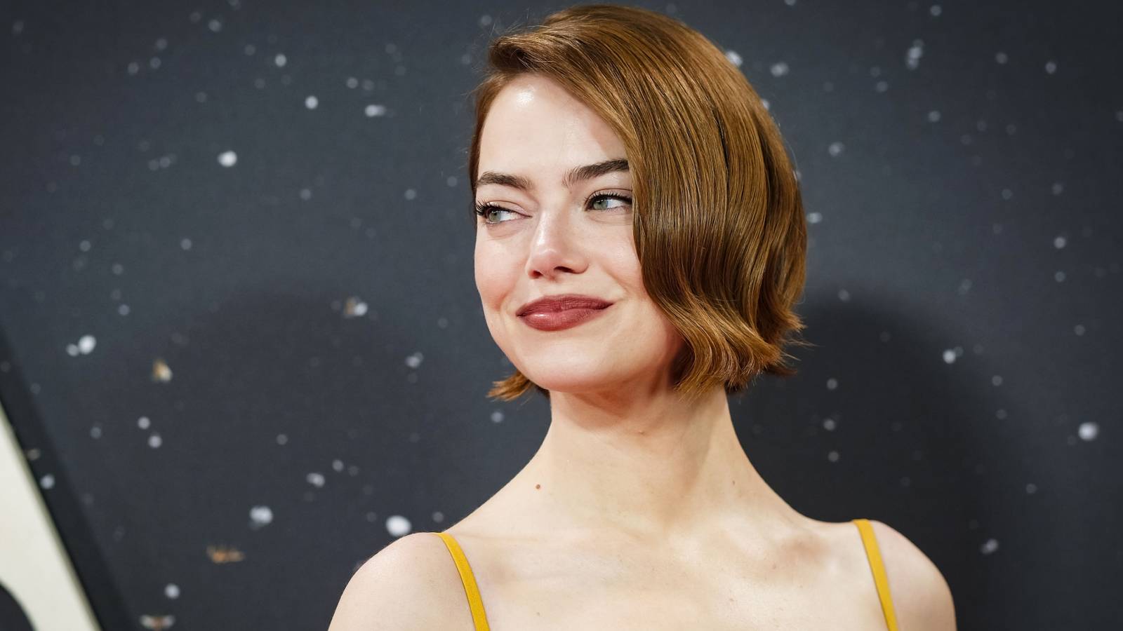 Emma stone smiling over her shoulder at a red carpet event