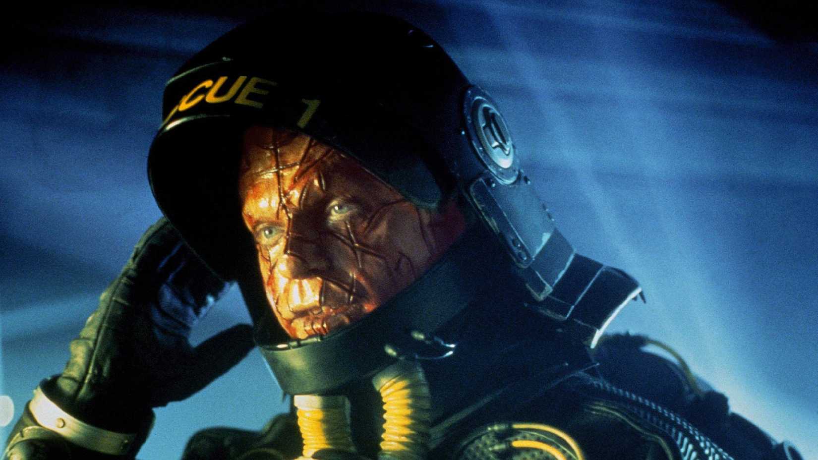 Sam Neill levanta o visor de seu traje espacial para revelar um rosto com cicatrizes em Event Horizon.