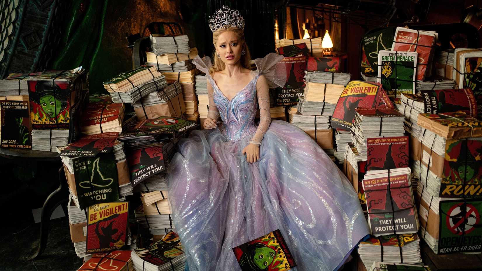 glinda in a ballgown and tiara looking dismayed while surrounded by anti elphaba propaganda in wicked for good