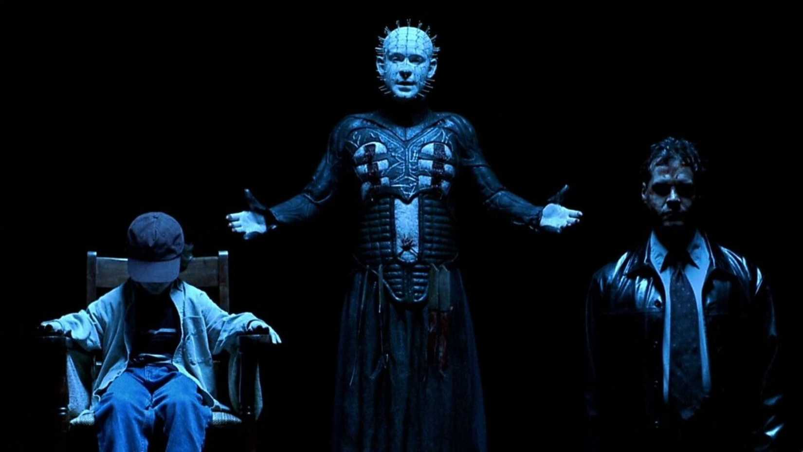 Pinhead está ao lado de uma criança e um homem em um vazio escuro em Hellraiser Inferno