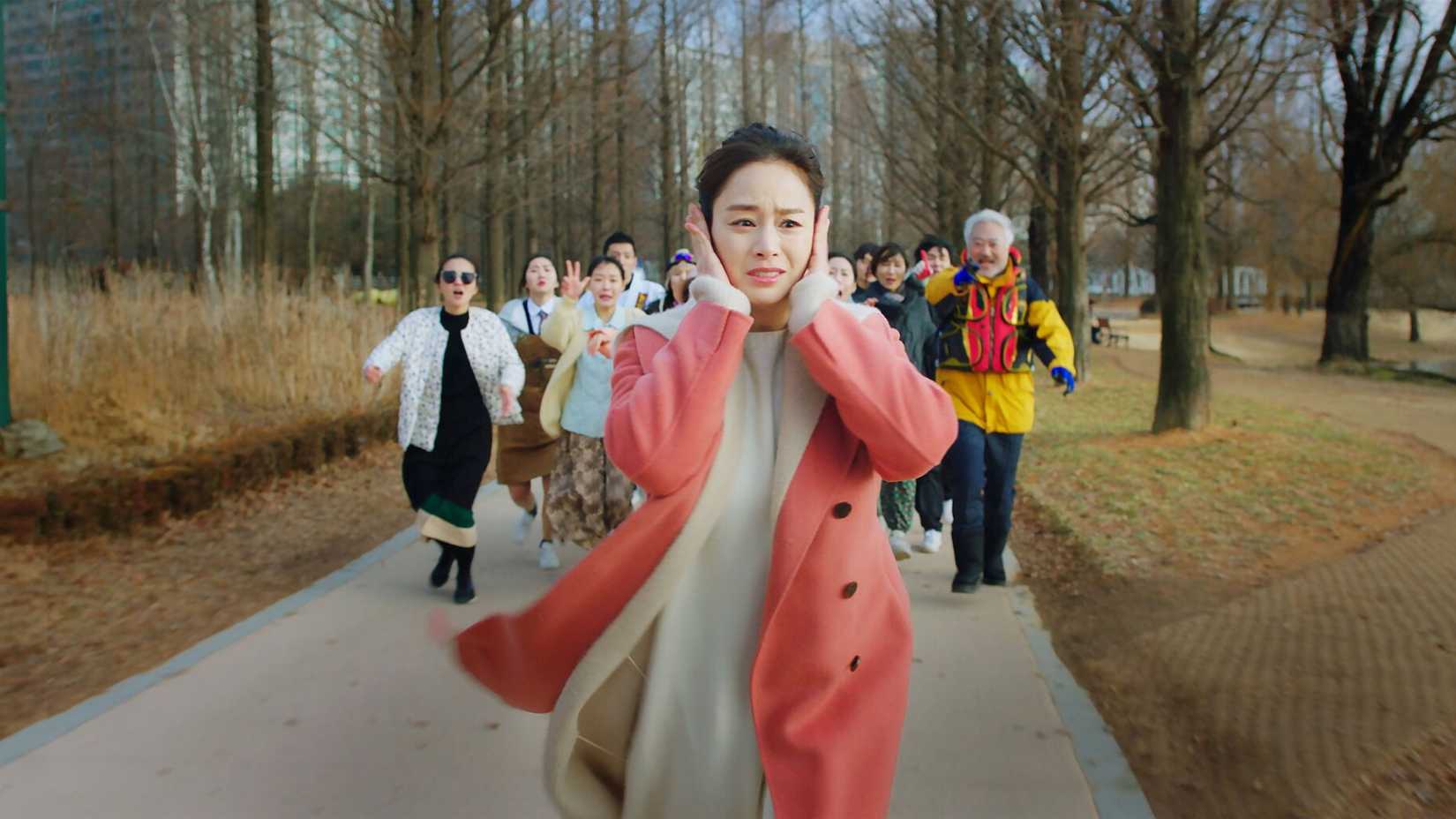 Uma mulher fugindo de uma multidão com os ouvidos tampados no K-drama Hi Bye, Mama!