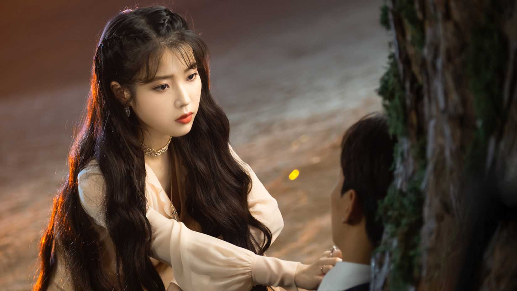 Uma mulher colocando a mão no coração de um homem encostado em uma árvore no K-drama Hotel del Luna.