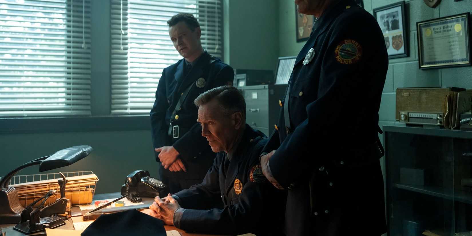 Clint Bowers (Peter Outerbridge) em seu escritório ladeado por dois policiais em It: Welcome to Derry.