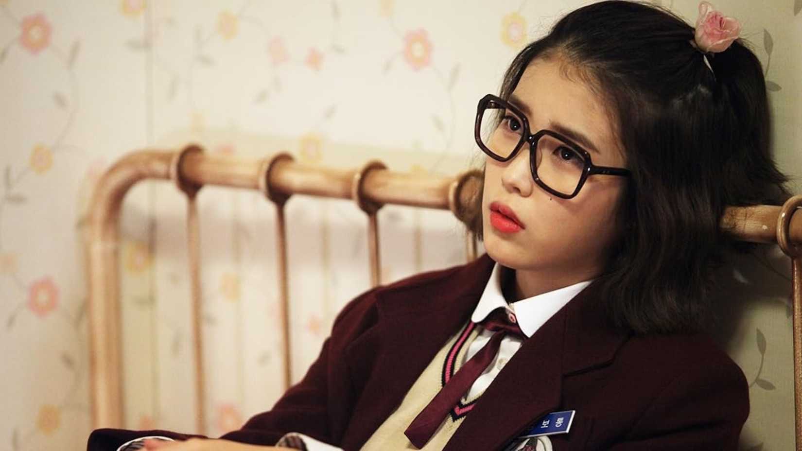 Uma estudante sentada na cama com uma expressão de desaprovação em Bel Ami.