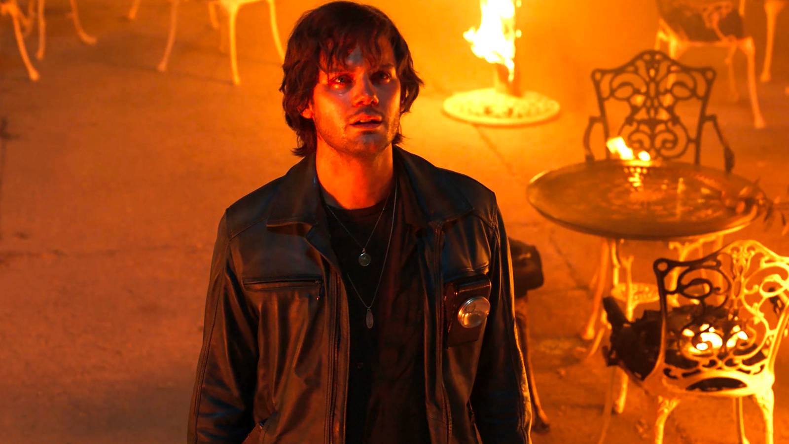 Jeremy Irvine's James with tears in his eyes looking up at something with furniture on fire around him in Return to Silent Hill