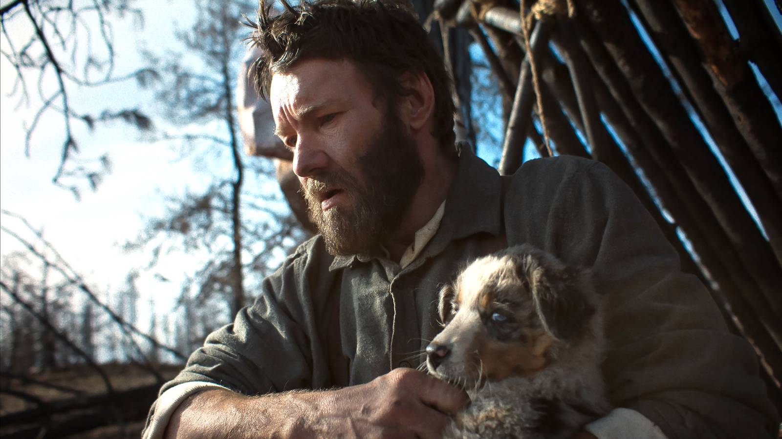 Joel Edgerton's Robert looking concerned while holding a puppy in Train Dreams