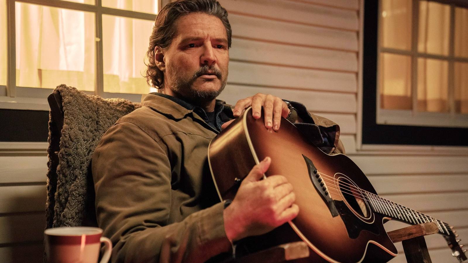 Pedro Pascal as Joel sitting on a porch holding a guitar in The Last of Us season 2