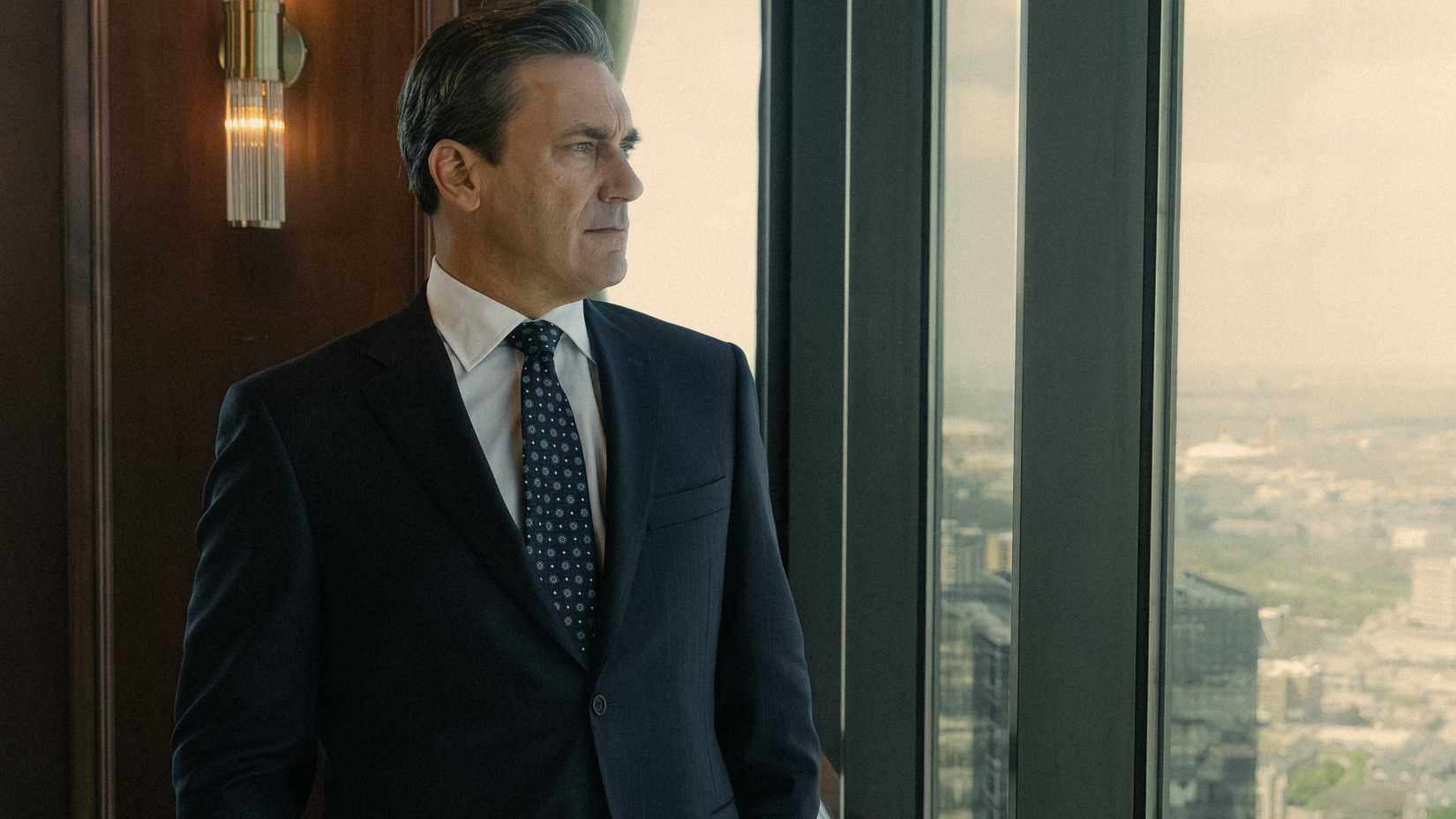 Jon Hamm gazes out a window with a pensive look in a scene from Landman season 1.