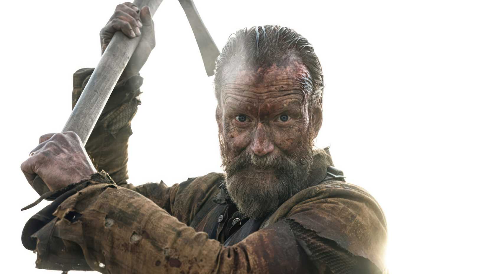 Jorma Tommila looks directly into the camera while raising a pickaxe above his head in a scene from Sisu