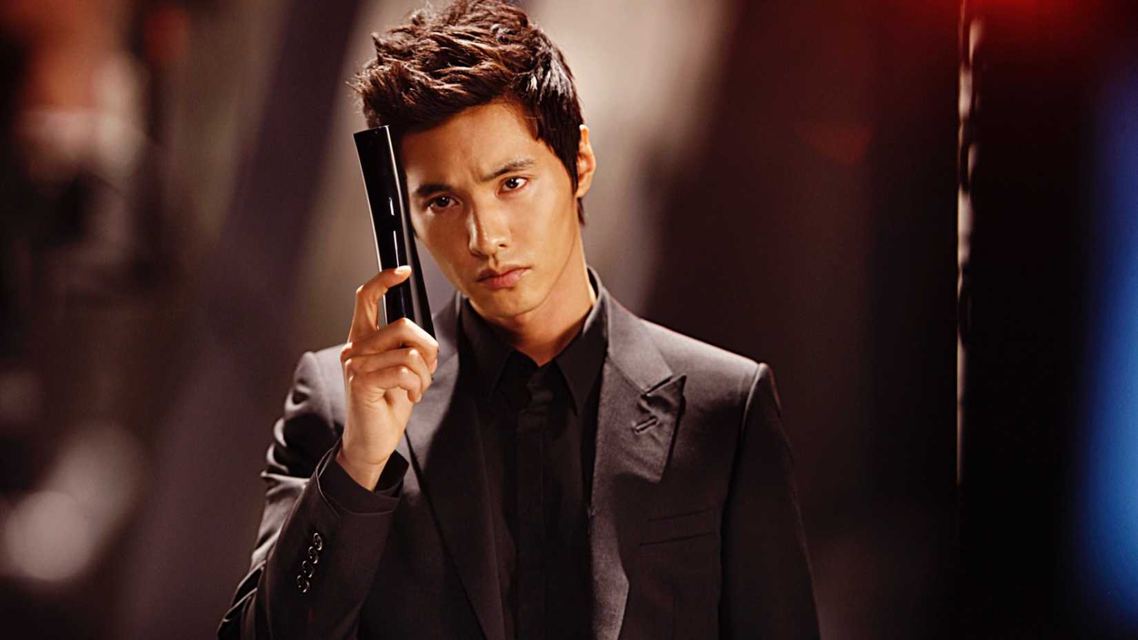 Won Bin segurando uma arma em um terno escuro.