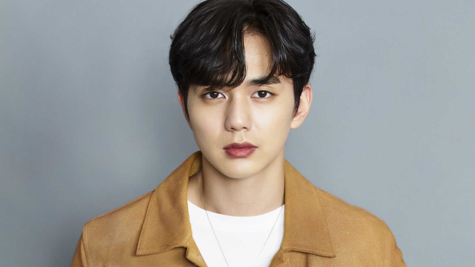 Yoo Seung-ho em uma jaqueta bege em frente a um fundo cinza.
