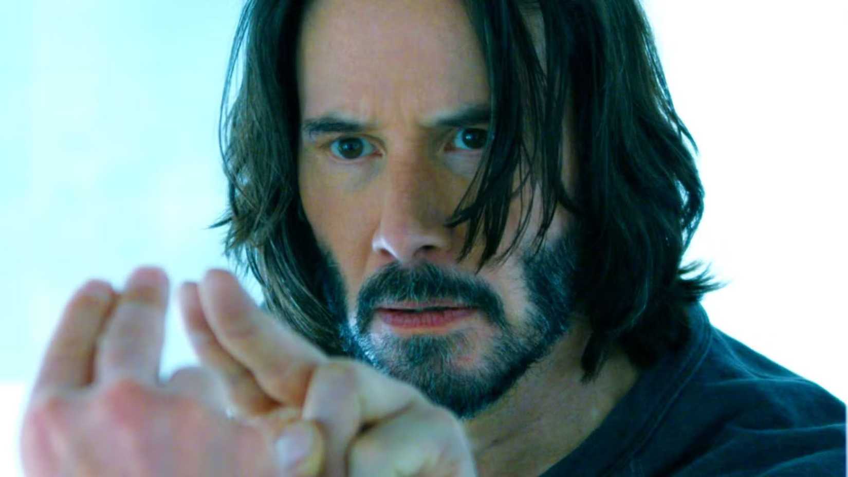 Keanu Reeves as Neo holding two fingers up to a mirror in The Matrix Resurrections