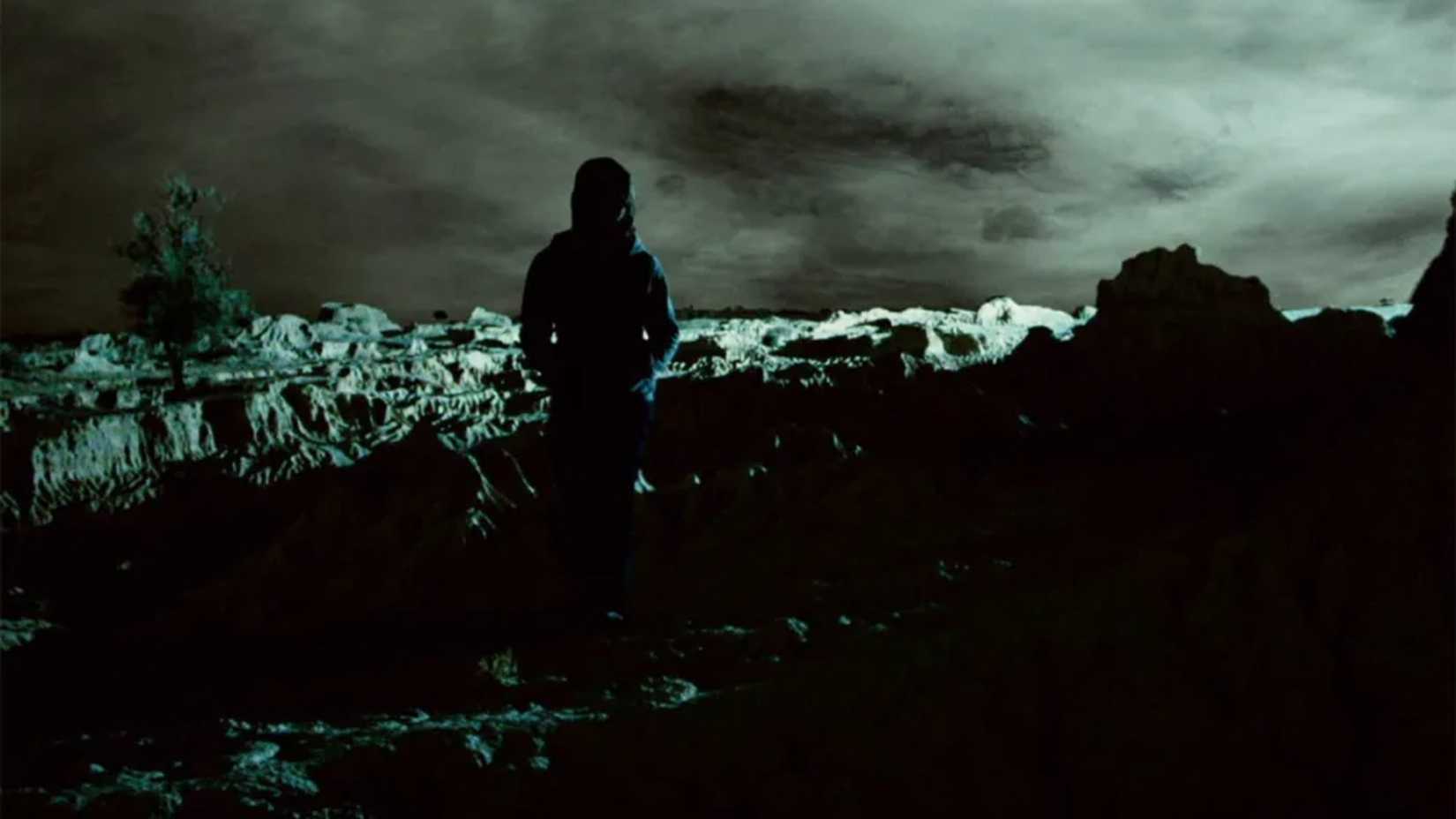 Uma mulher é silhuetada contra a paisagem escura em Lake Mungo