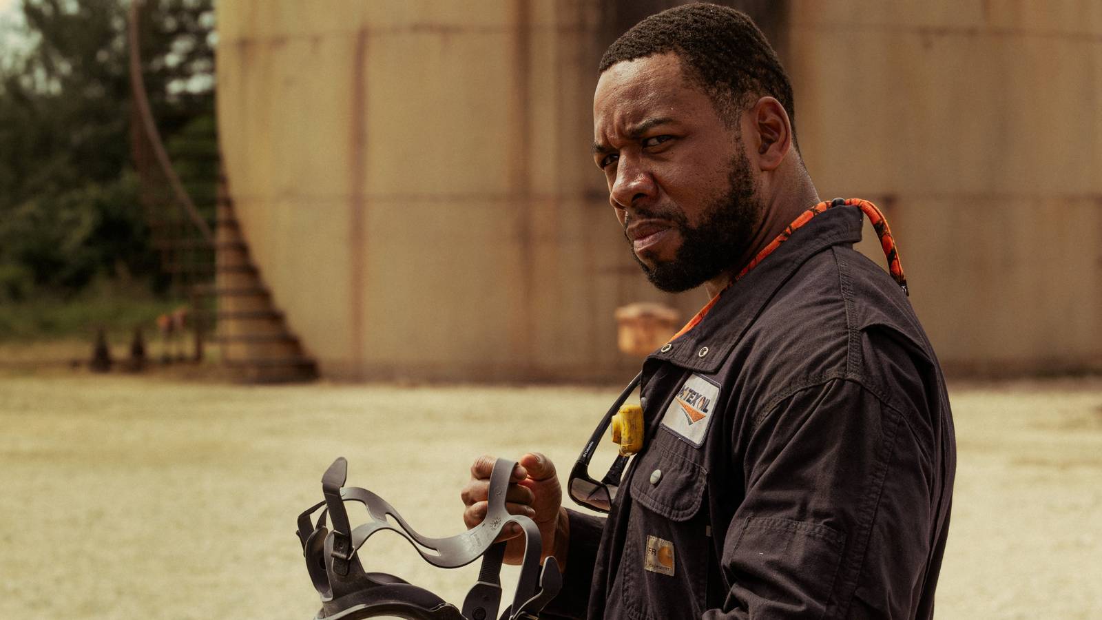 Boss (Mustafa Speaks) holding a gas mask and looking angry next to an oil tanker in Landman season 2, episode 3