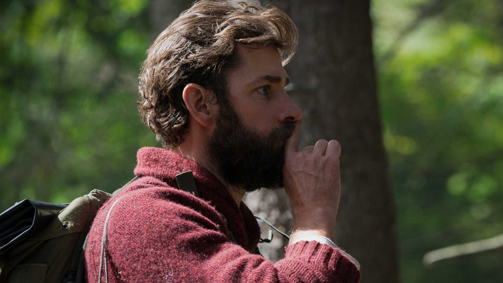 John Krasinski as Lee Abbott putting a finger to his mouth in front of a tree, signaling someone to be quiet in A Quiet Place