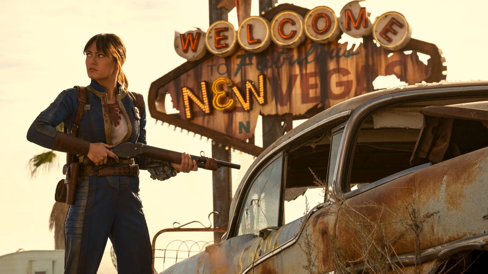 Lucy Maclean (Ella Purnell) holding a gun and standing in front of the Fallout New Vegas sign