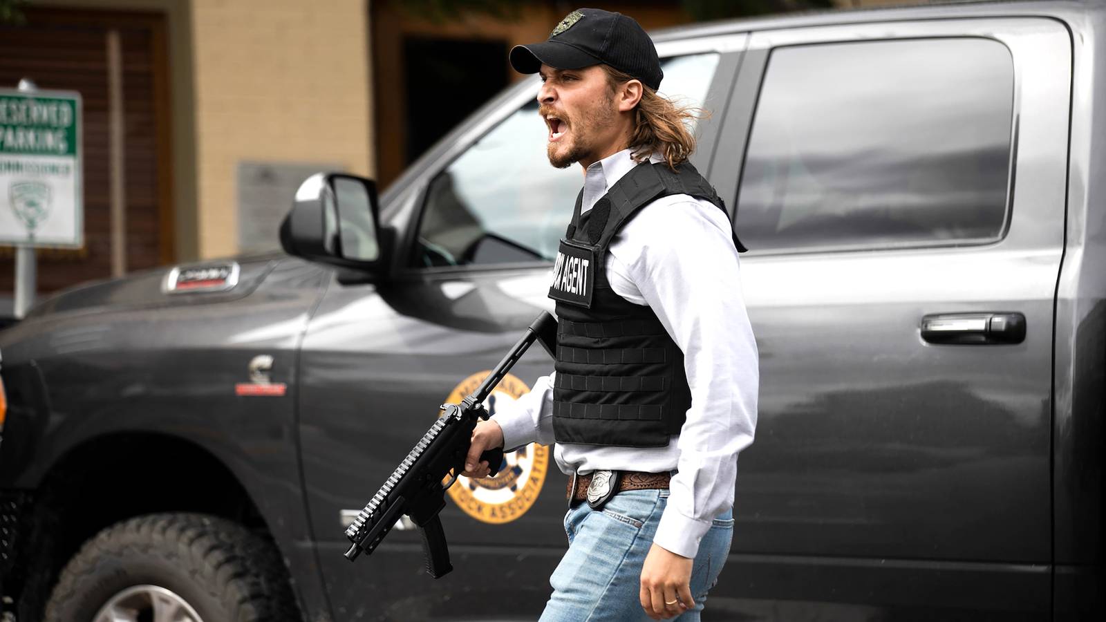 Luke Grimes as Kayce shouting while walking down a street with an assault rifle in Yellowstone