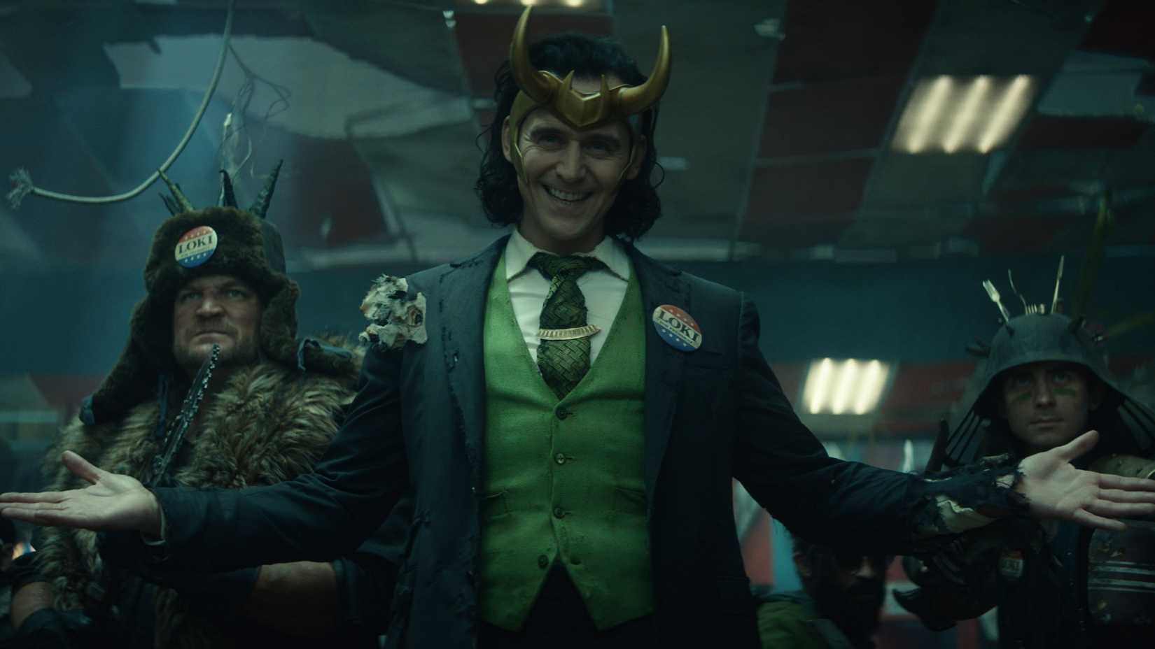 President Loki raising his hands and smiling in front of his followers in Loki