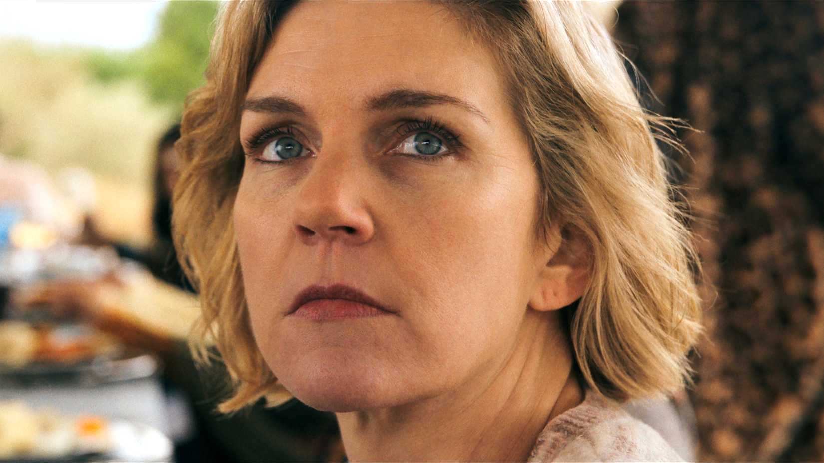 Rhea Seehorn como Carol em Pluribus, olhando por cima do ombro com seriedade.