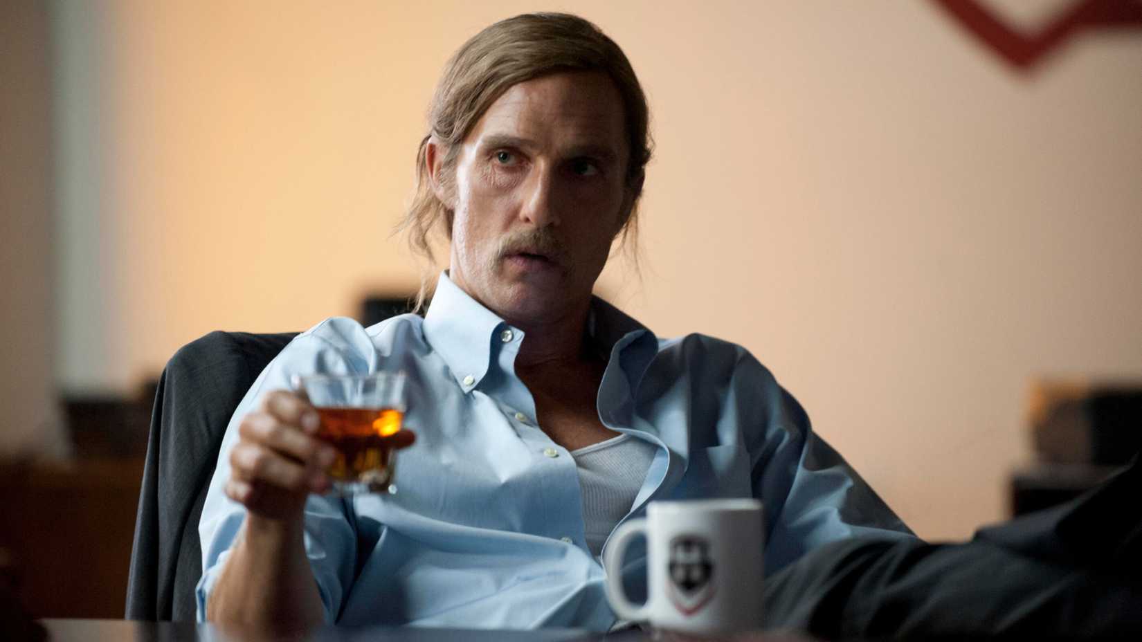 rust cohle sitting down and raising a glass of liquor in true detective