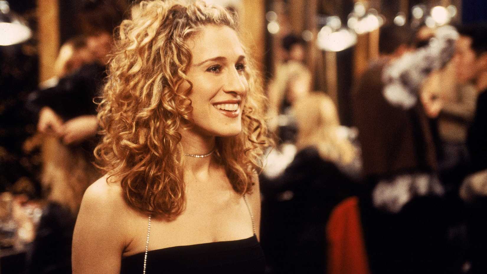 Sarah Jessica Parker como Carrie Bradshaw sorrindo em uma festa em Sex and the City