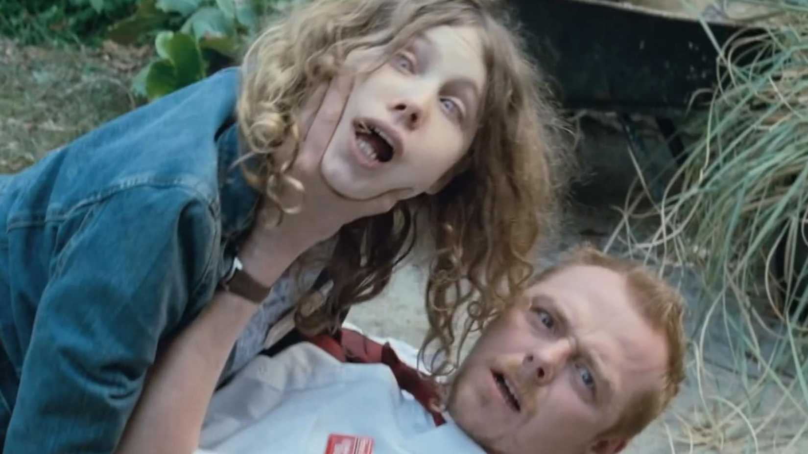 Simon Pegg posando para uma foto com um zumbi no chão em Todo Mundo Quase Morto