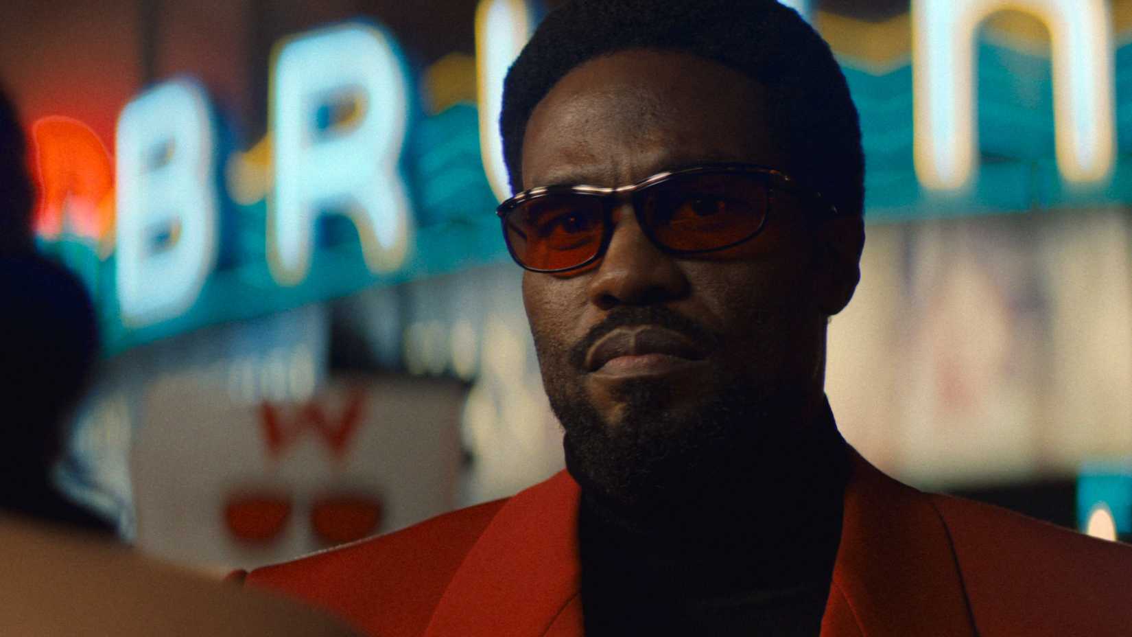 Simon Williams de terno vermelho e óculos escuros em Wonder Man