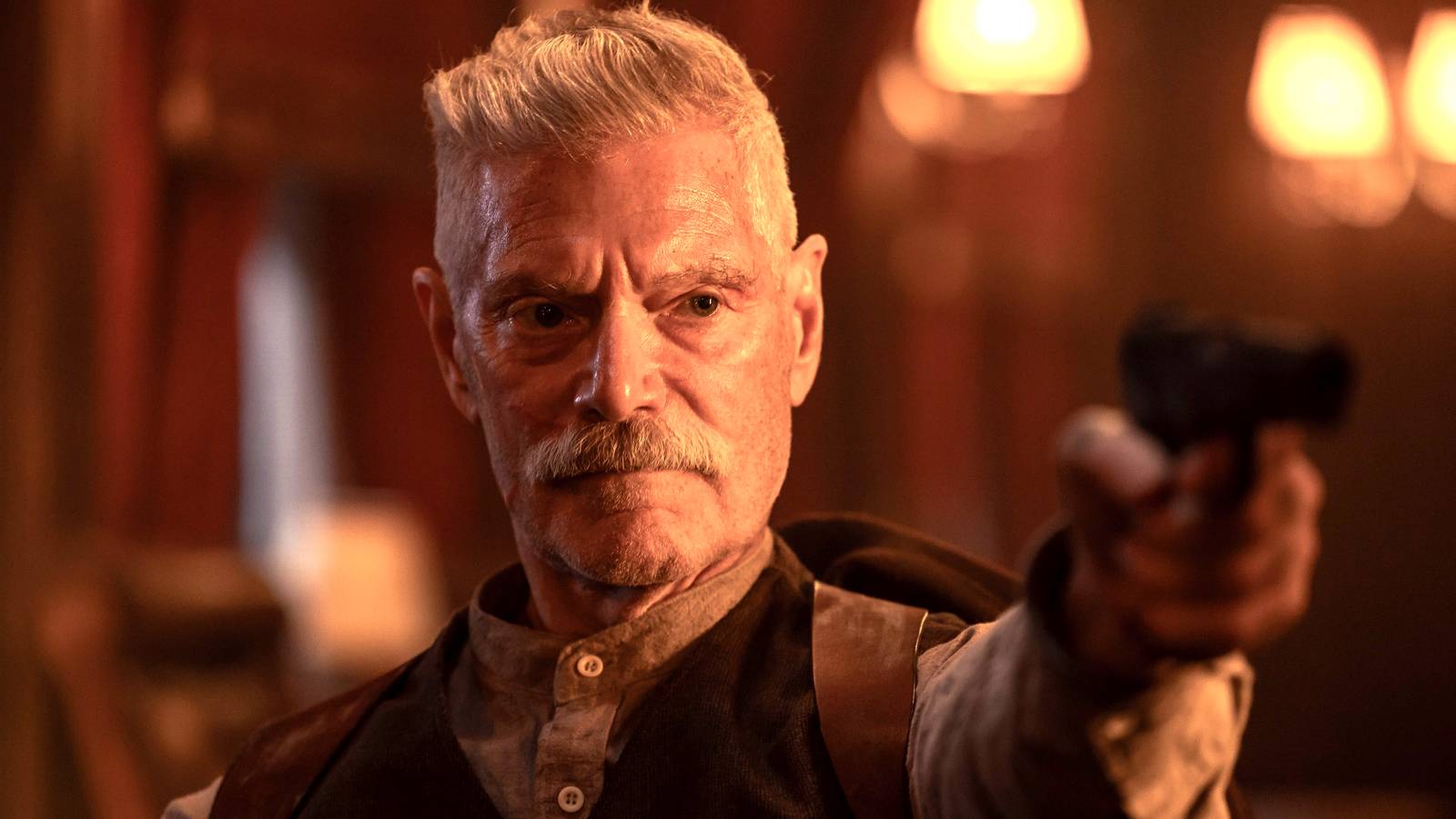 Stephen Lang's Igor aiming a gun while sitting down in Sisu: Road to Revenge