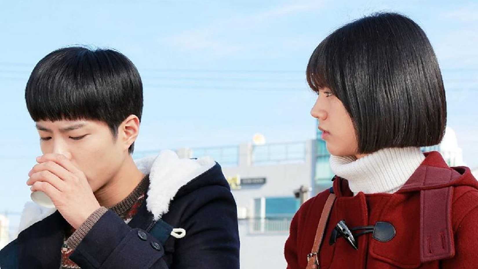 Uma garota de casaco vermelho observando um garoto beber de um copo em Reply 1988.