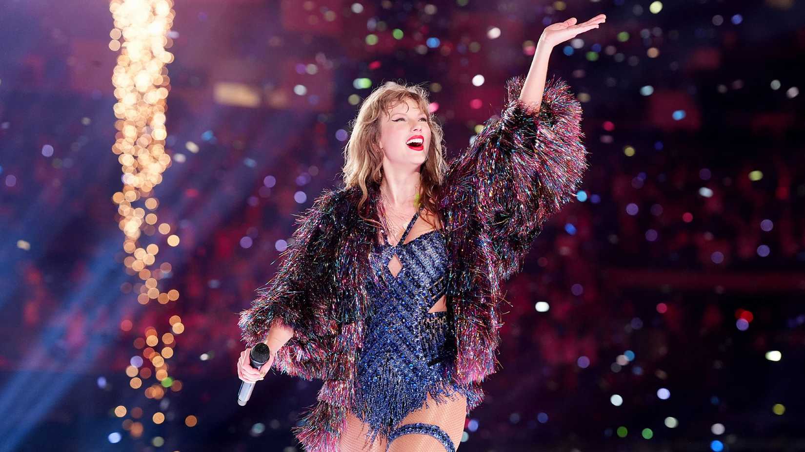 Taylor Swift posing in a rainbow fringe jacket on the Eras Tour.