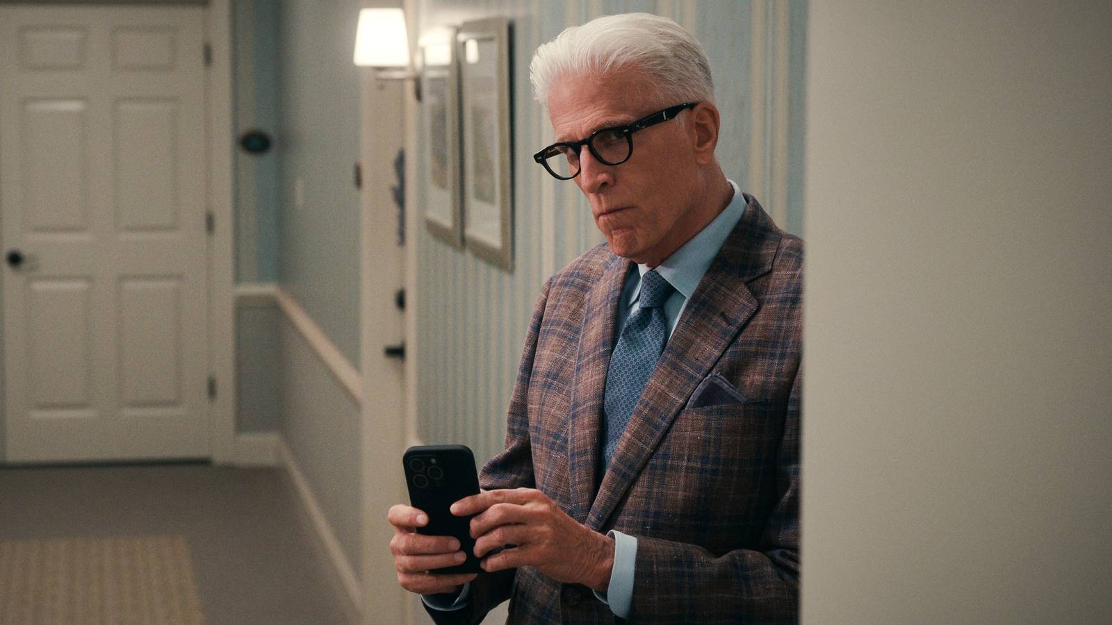 Ted Danson in A Man On the Inside holding up a phone and looking suspicious