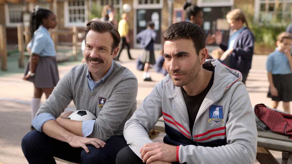Ted Lasso and Roy Kent sitting together and smiling in Ted Lasso season 3