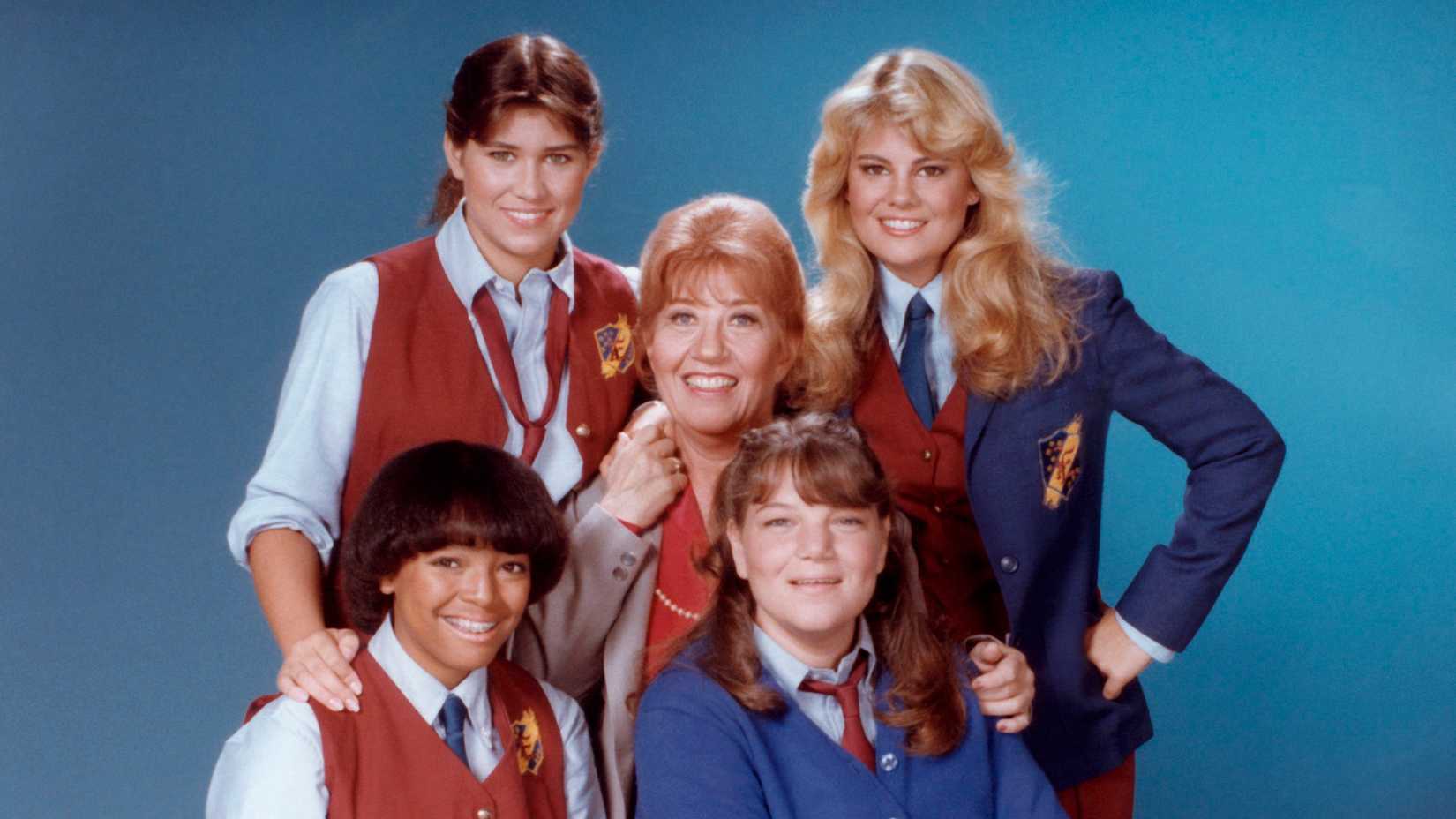 The Facts Of Life cast posing in their uniforms against a blue background.